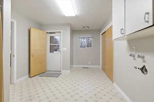 Laundry area featuring light flooring, a textured ceiling, and cabinet storage space. This area features new lighting and 2 exits to the outside
