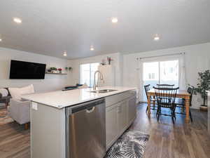 Kitchen featuring stainless steel dishwasher, a kitchen island with sink, gray cabinetry, dark wood-type flooring, and open floor plan