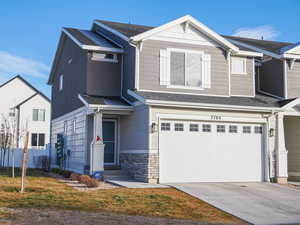 View of front of property featuring a garage, concrete driveway, stone siding, and a front yard