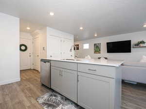 Kitchen featuring open floor plan, dark wood-style floors, gray cabinetry, stainless steel dishwasher, and a kitchen island with sink