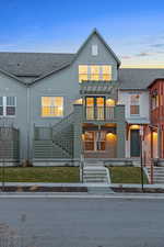 View of front of home featuring roof with shingles, a balcony, stucco siding, a front lawn, and stairway