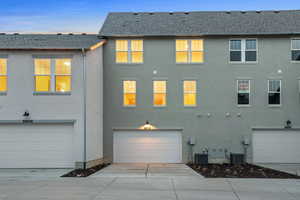 Back of property at dusk featuring driveway, roof with shingles, and stucco siding