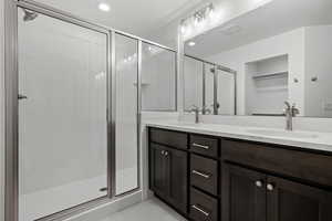 Full bathroom featuring double vanity, a walk in closet, a stall shower, recessed lighting, and a textured ceiling