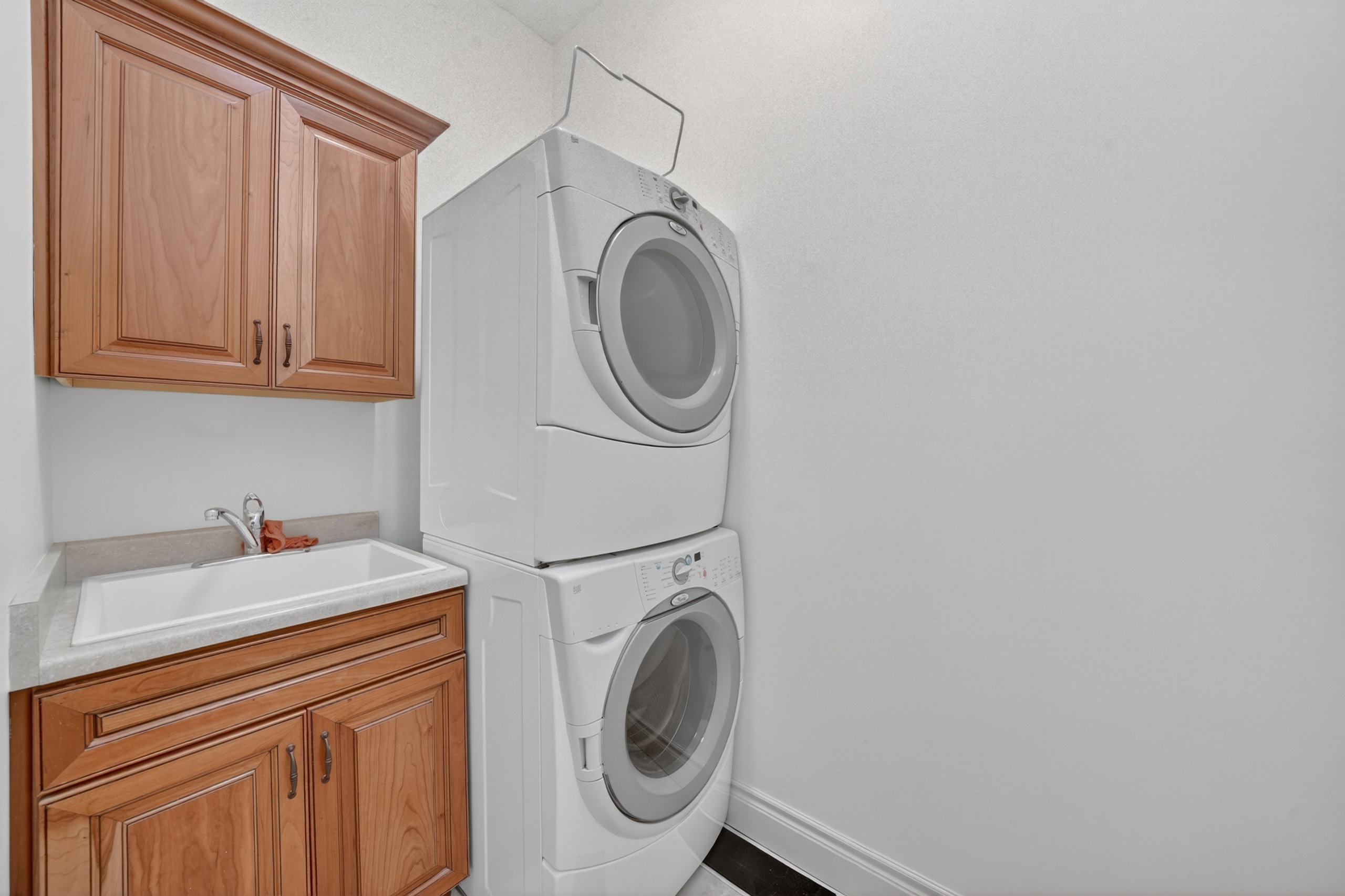 Laundry area featuring a stacked washer and dryer, wood cabinetry, a utility sink, and light-toned countertops