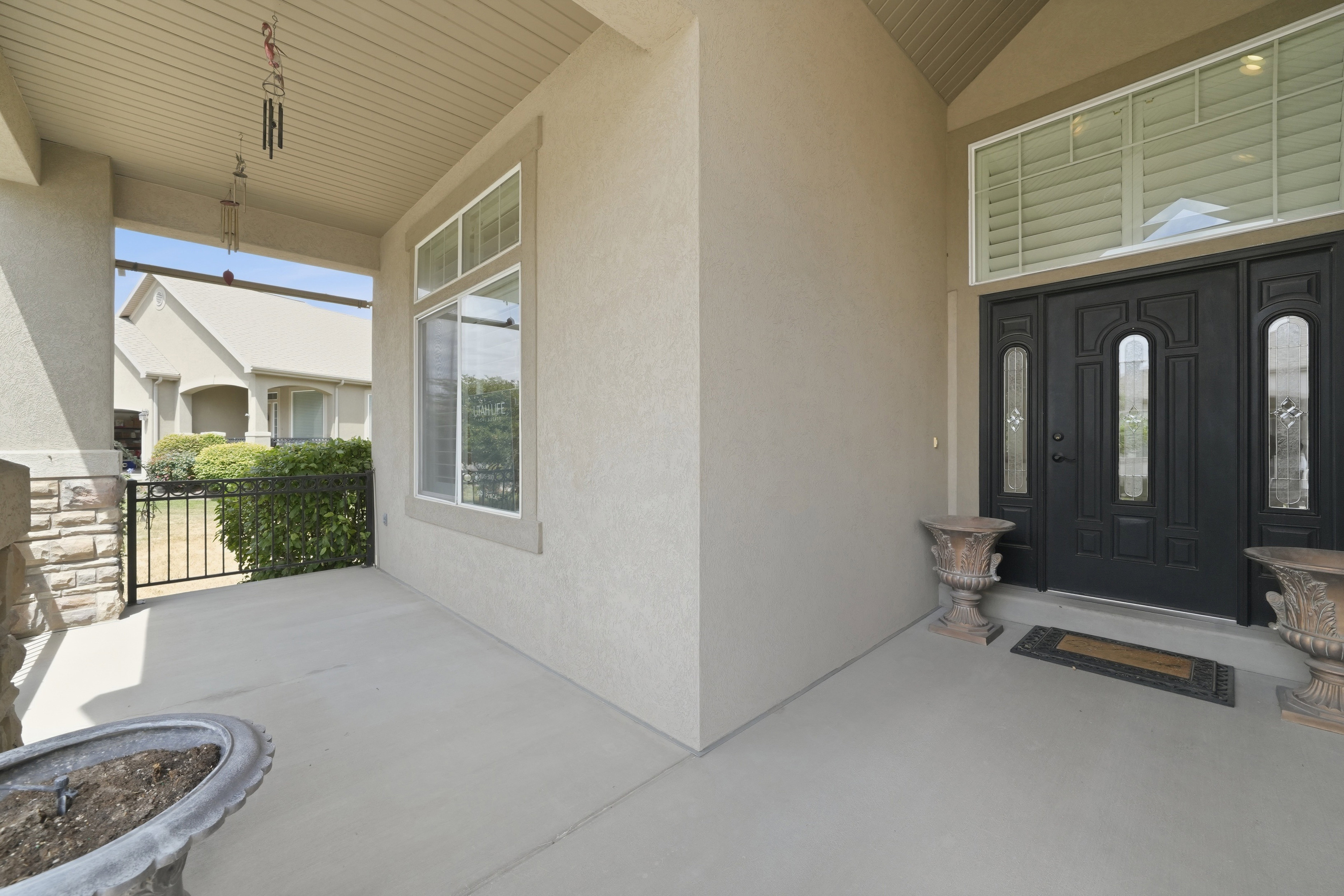Entryway featuring a double door with decorative glass inserts, a transom window with plantation shutters, and a covered porch with a stone column base