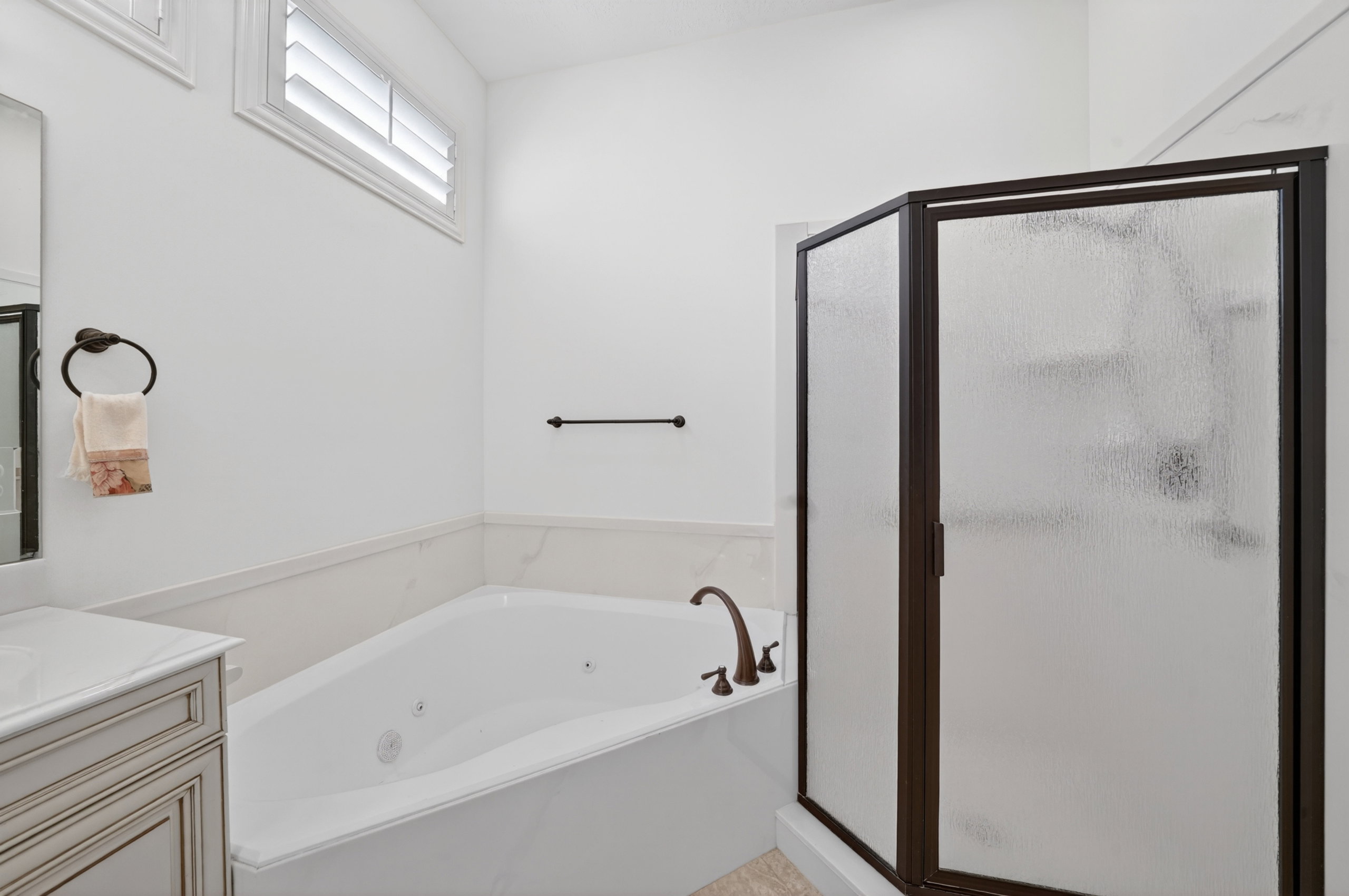 Bathroom featuring a white jetted soaking tub with bronze fixtures, a framed glass shower enclosure, and a vanity with a white countertop and integrated sink