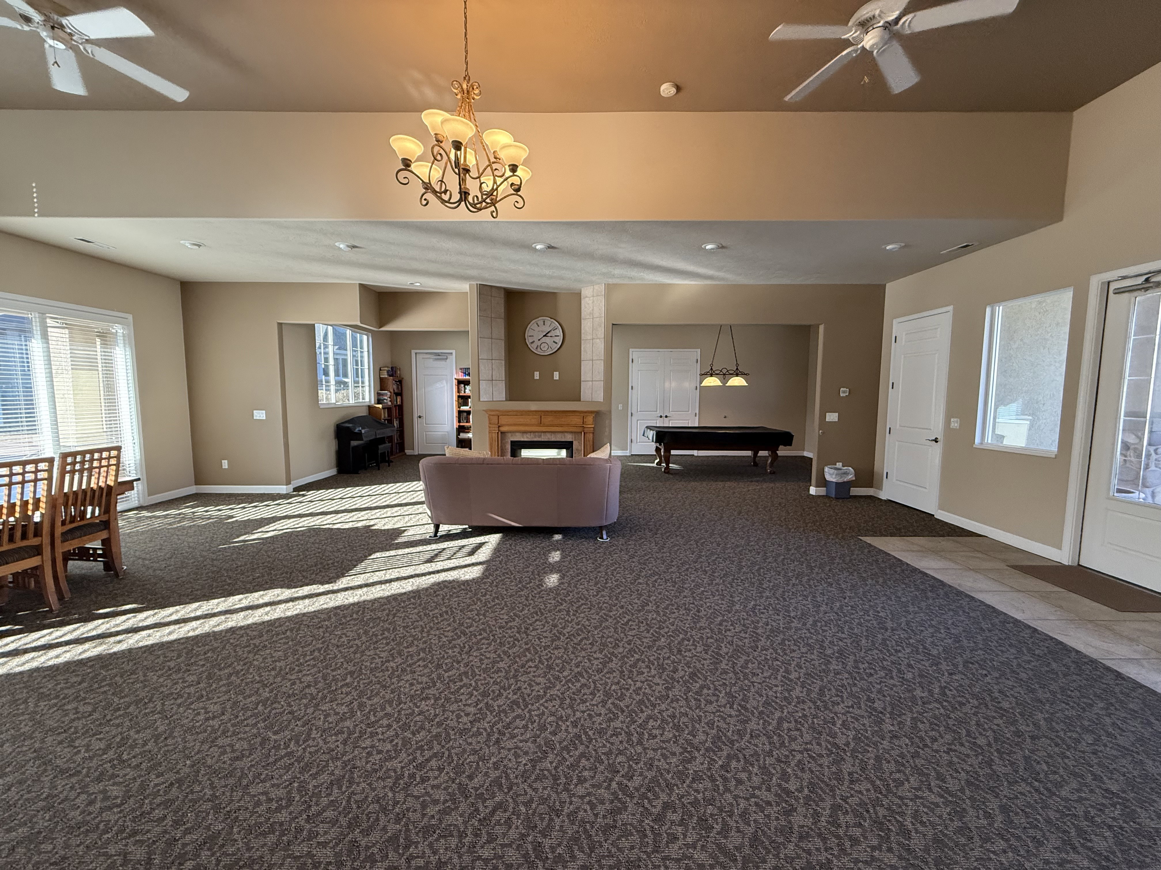 Clubhouse living area featuring a ceiling fan, a fireplace, carpet floors, and a chandelier