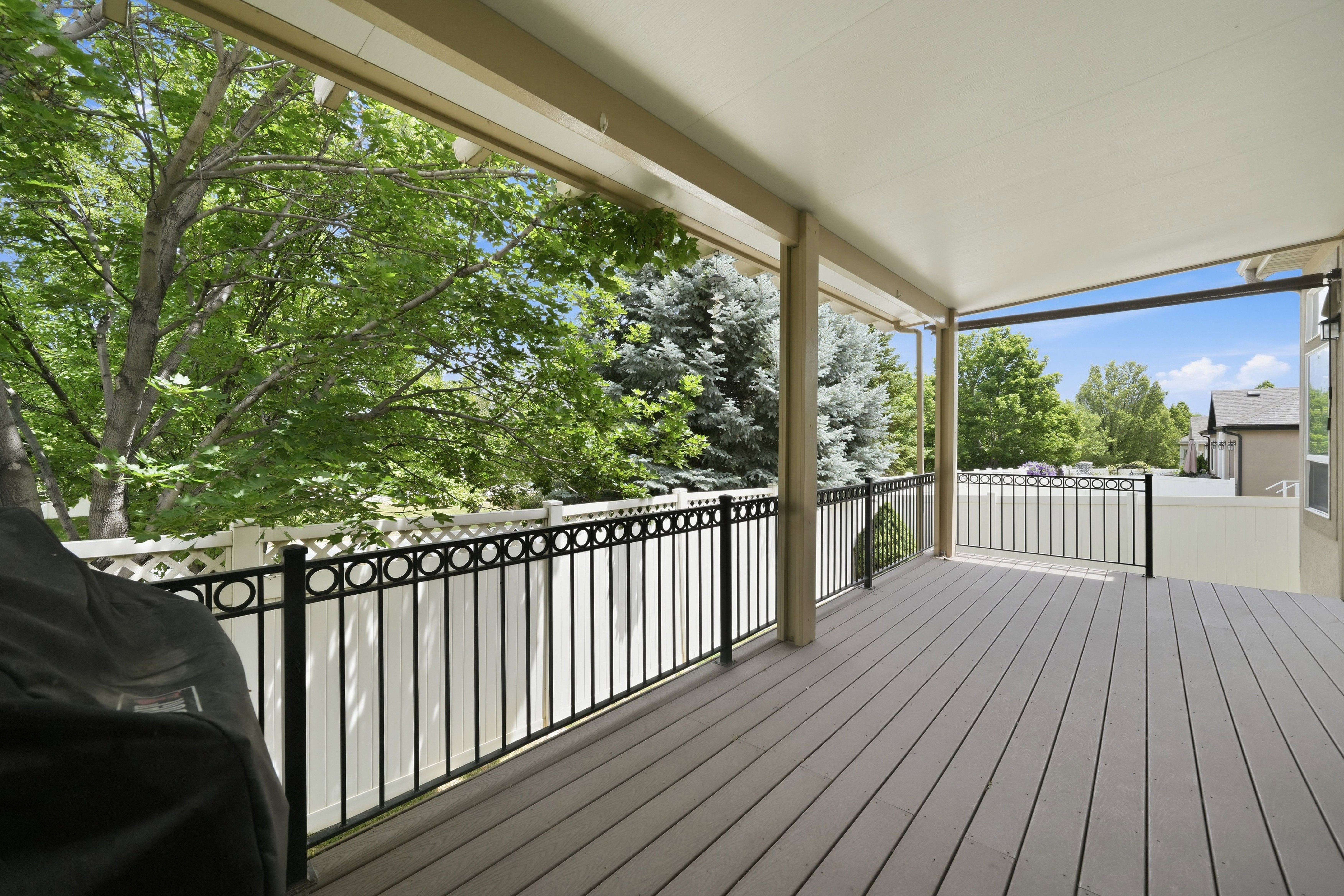 Spacious covered deck featuring composite decking, black metal railings with circular accents, and white privacy fencing