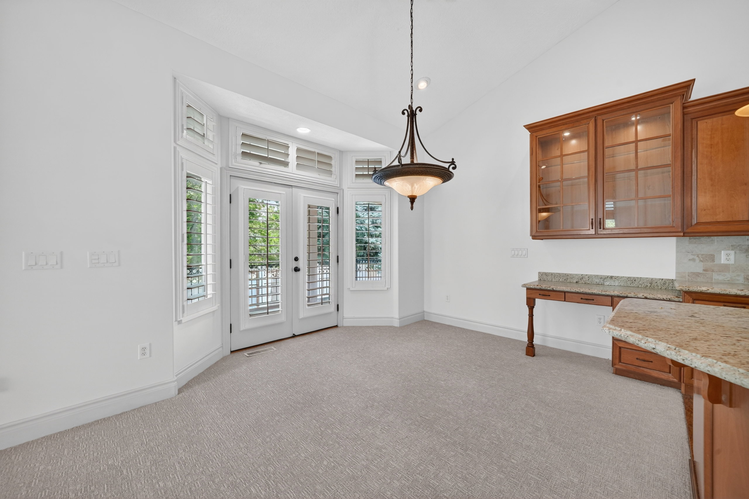 Bright dining area featuring French doors with transom windows and plantation shutters, a decorative chandelier, and built-in cabinetry with glass fronts