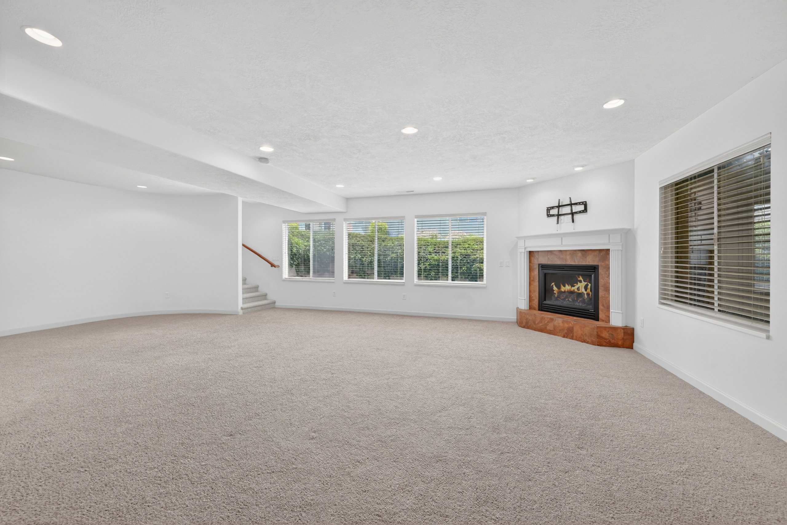 Spacious room featuring neutral carpeting and a corner fireplace with a white mantel and stone surround