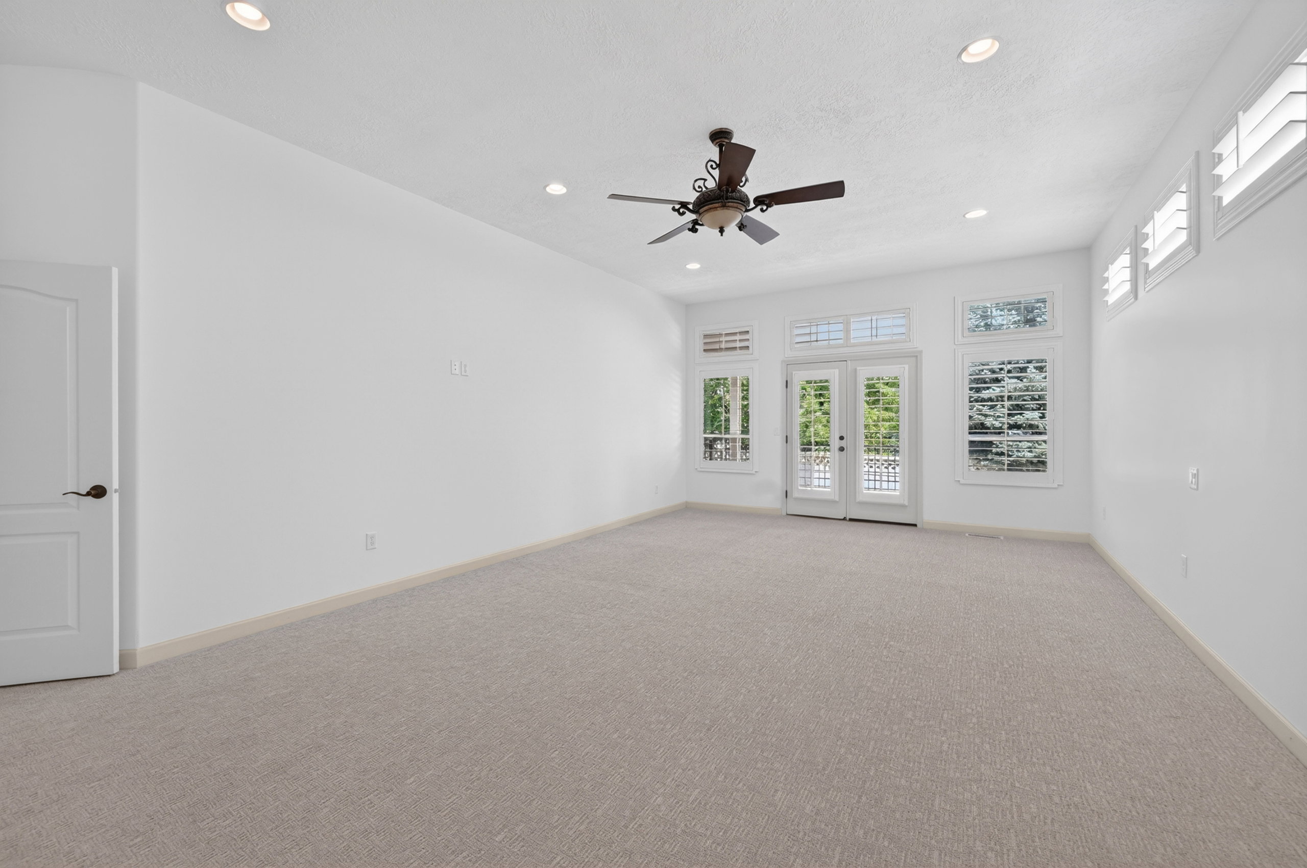 Spacious room featuring light-toned carpeting, ample natural light from multiple windows, and a ceiling fan with integrated lighting