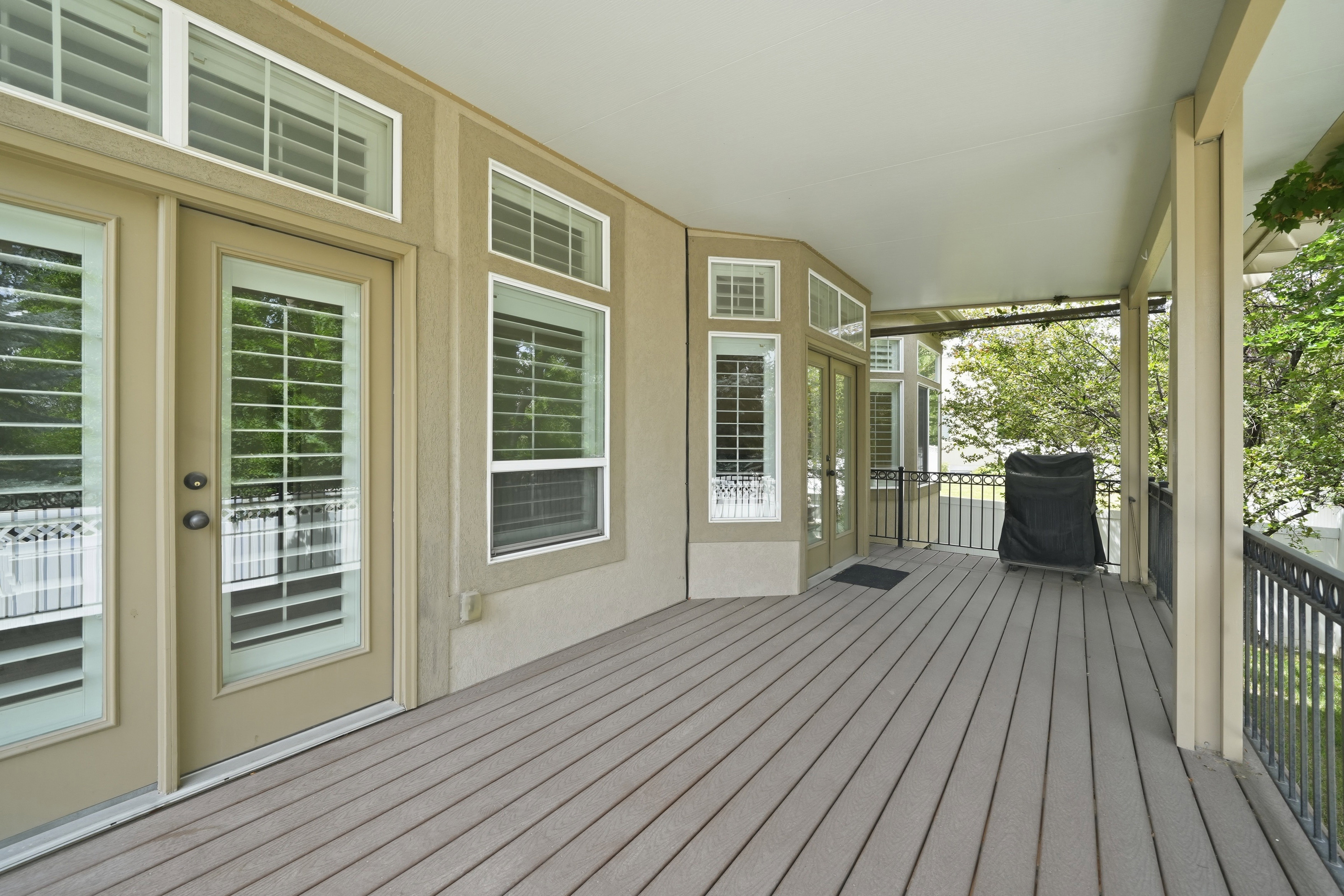 Spacious covered deck featuring composite flooring, recessed lighting, multiple access points, and black wrought iron railings