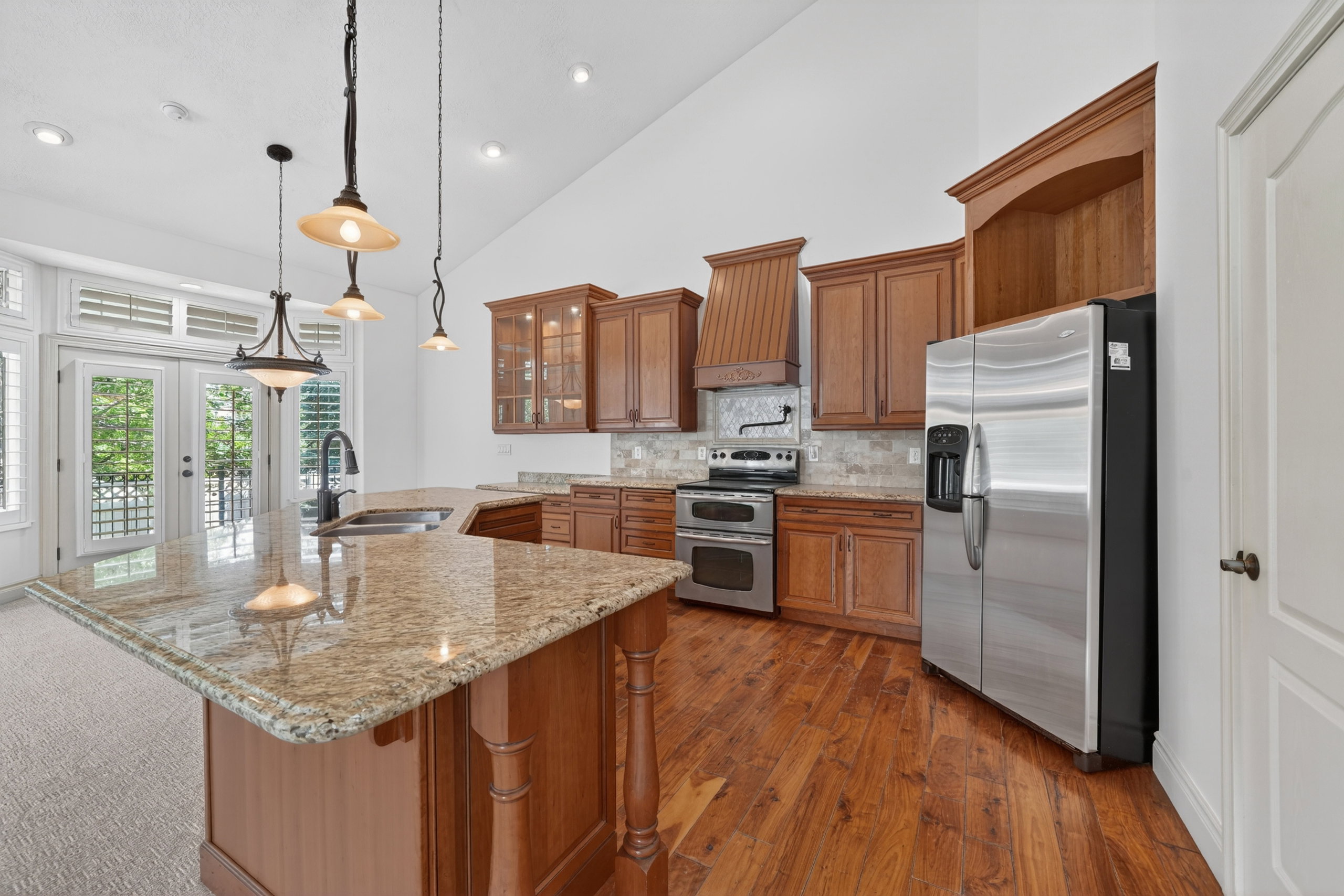 Kitchen featuring a large central island with a granite countertop, wood-finish flooring, vaulted ceilings, and stainless steel appliances