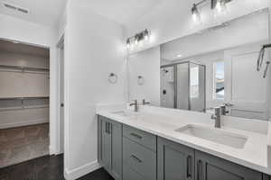 Full bath featuring double vanity, a stall shower, and a walk in closet