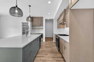 Kitchen featuring range with gas stovetop, light wood finished floors, a center island with sink, light stone counters, and pendant lighting