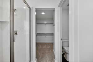 Full bath featuring a spacious closet, a marble finish shower, light carpet, and recessed lighting