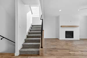 Stairway featuring wood finished floors, a glass covered fireplace, and recessed lighting