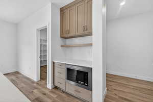 Bar area featuring stainless steel microwave, open shelves, light wood-style flooring, tasteful backsplash, and light stone counters