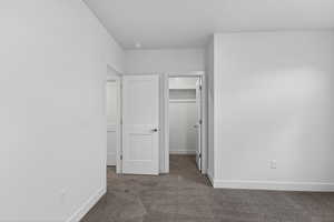 Unfurnished bedroom with a walk in closet and dark carpet