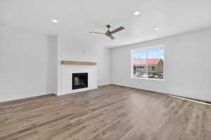 Unfurnished living room featuring ceiling fan, light wood-style floors, a glass covered fireplace, and recessed lighting