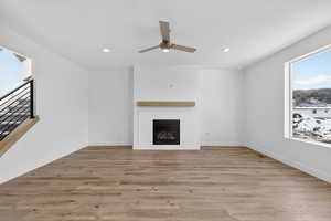 Unfurnished living room featuring plenty of natural light, light wood-type flooring, ceiling fan, a glass covered fireplace, and recessed lighting