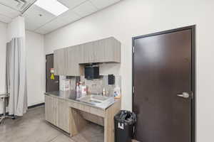 Kitchen featuring finished concrete floors, stainless steel countertops, decorative backsplash, light brown cabinets, and a paneled ceiling
