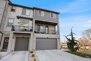 View of front of home with a balcony, stone siding, driveway, and a garage