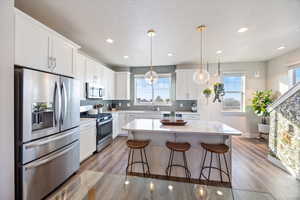 Kitchen featuring stainless steel appliances, a kitchen bar, pendant lighting, white cabinets, and a center island