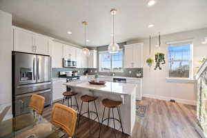Kitchen with appliances with stainless steel finishes, a kitchen bar, decorative backsplash, white cabinetry, and recessed lighting