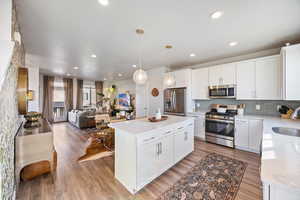 Kitchen featuring white cabinets, appliances with stainless steel finishes, decorative light fixtures, a center island, and open floor plan