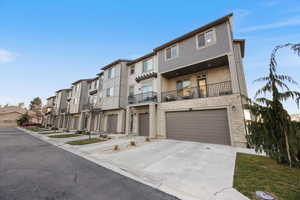 View of front of property with driveway, a balcony, a garage, a residential view, and stone siding