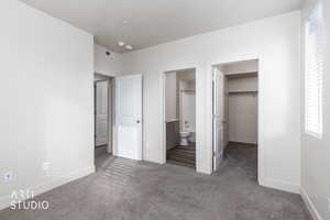 Unfurnished bedroom featuring dark carpet, a walk in closet, and ensuite bathroom