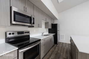 Kitchen with appliances with stainless steel finishes, dark wood-type flooring, modern cabinets, dark brown cabinetry, and light stone countertops