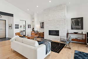Living area featuring a fireplace, light wood-style flooring, recessed lighting, and high vaulted ceiling