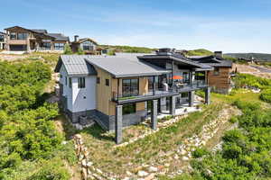 Rear view of property with a patio area, a balcony, a metal roof, stone siding, and a residential view