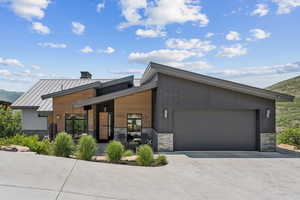Modern home with stone siding, concrete driveway, a porch, a standing seam roof, and a metal roof