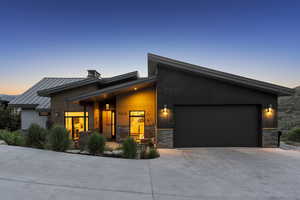 Contemporary home featuring stone siding, driveway, a metal roof, a standing seam roof, and a garage