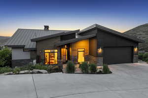 View of front of property featuring stone siding, a standing seam roof, concrete driveway, a metal roof, and an attached garage