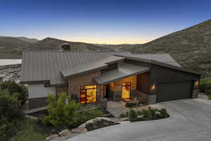 Contemporary home with stone siding, a standing seam roof, a mountain view, concrete driveway, and a metal roof