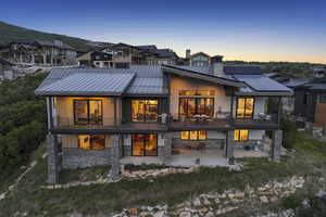 Back of house at dusk with stone siding, roof mounted solar panels, a standing seam roof, a patio, and a chimney
