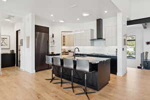 Kitchen with dark cabinets, an island with sink, a kitchen bar, dark stone counters, and stainless steel refrigerator