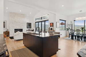 Kitchen featuring light wood-style flooring, a fireplace, modern cabinets, pendant lighting, and a kitchen island with sink