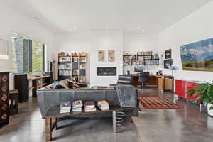 Living area featuring finished concrete floors, recessed lighting, a glass covered fireplace, and built in study area