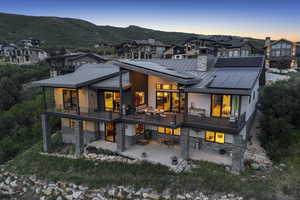 Back of house at dusk with a standing seam roof, stone siding, a patio, and a metal roof