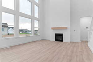 Unfurnished living room with light wood finished floors, a glass covered fireplace, and a high ceiling