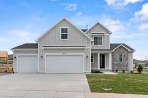 View of front facade with board and batten siding, concrete driveway, a front lawn, roof with shingles, and stone siding