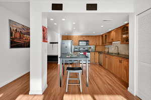 Dine-in kitchen with stainless steel appliances, glass insert cabinets, natural wood cabinetry, and recessed lighting