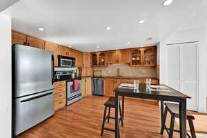 Dine-in kitchen with stainless steel appliances, glass insert cabinets, natural wood cabinetry, and recessed lighting