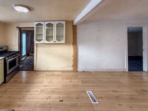 Kitchen featuring gas stove, a textured ceiling, glass insert cabinets, light wood-style flooring, and white cabinetry