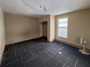 Unfurnished bedroom with a textured ceiling, a closet, and dark colored carpet